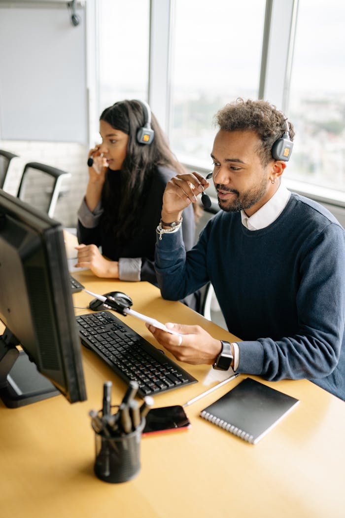 about-01 Two diverse call center agents working together at their desks with headsets in a bright office.